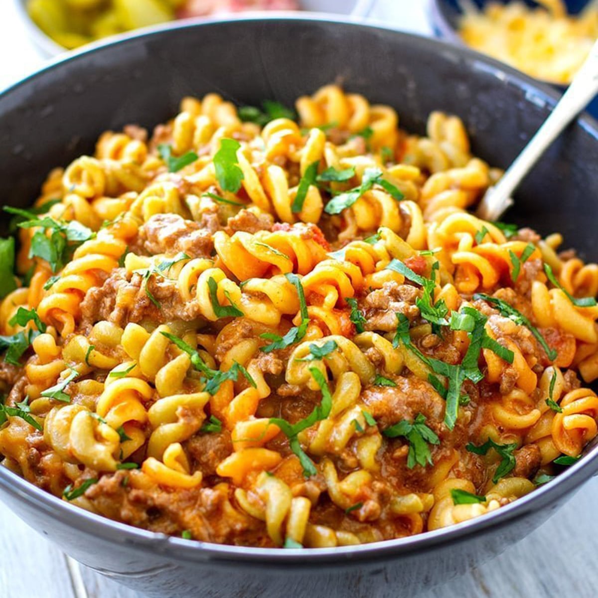 A close-up shot of a dark grey bowl filled with Instant Pot cheesy beef pasta, a creamy, savory dish made with cavatappi pasta and ground beef, garnished with fresh chopped parsley