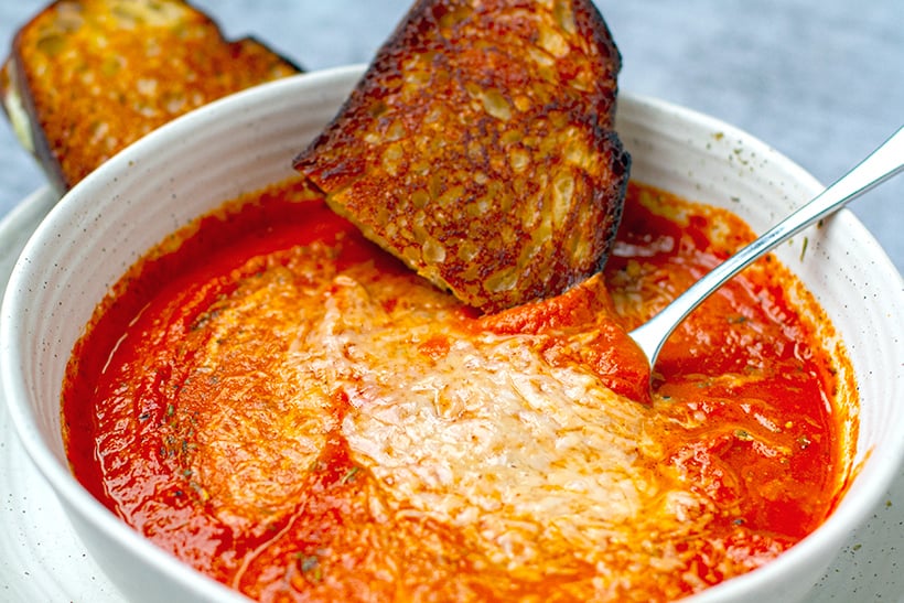 A bowl of tomato soup with Parmesan cheese and grilled cheese on the side.