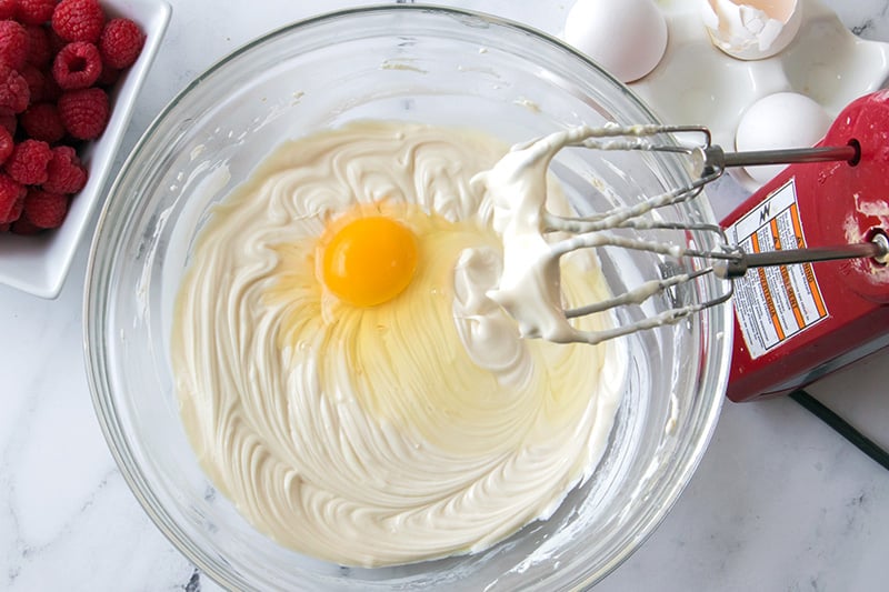 Adding eggs one at a time to the cheesecake filling