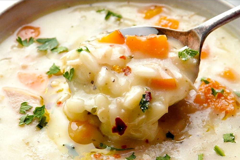 A spoon scooping creamy Lemon Chicken Orzo Soup from a bowl.