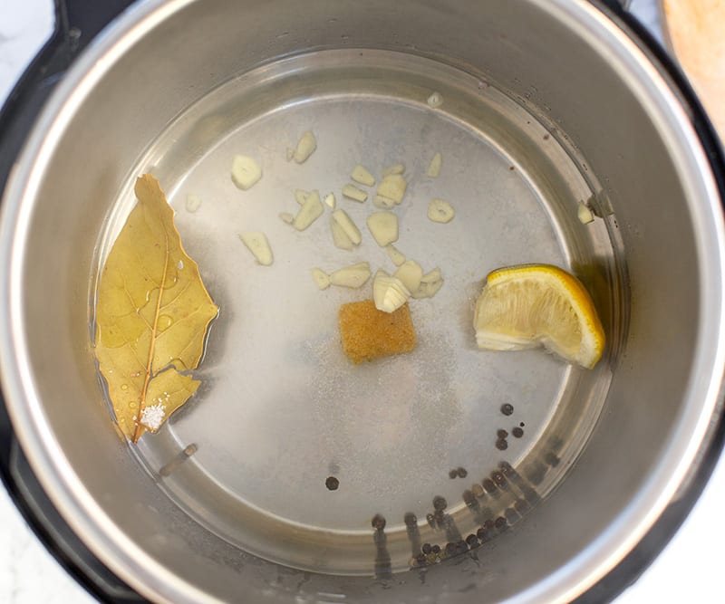 Water in the pot with garlic, lemon, pepper and bay leaf for poaching chicken