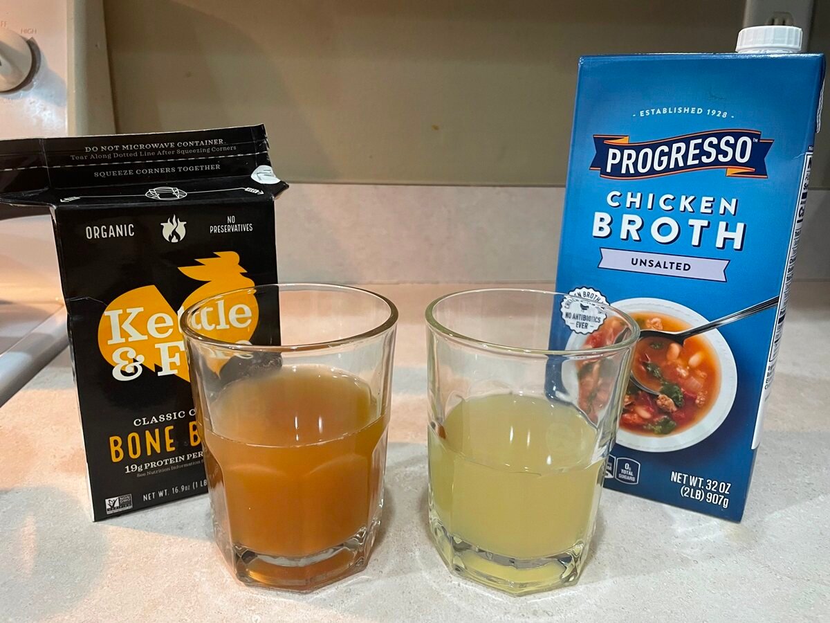 a box of Kettle and Fire Bone Broth and a box of Progresso. Two glasses of broth for comparison