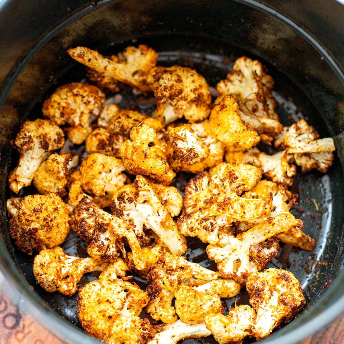 Golden-brown, crispy air fryer cauliflower florets seasoned with spices and served with lemon wedges on a white plate, perfect as quick and easy last minute potluck ideas.