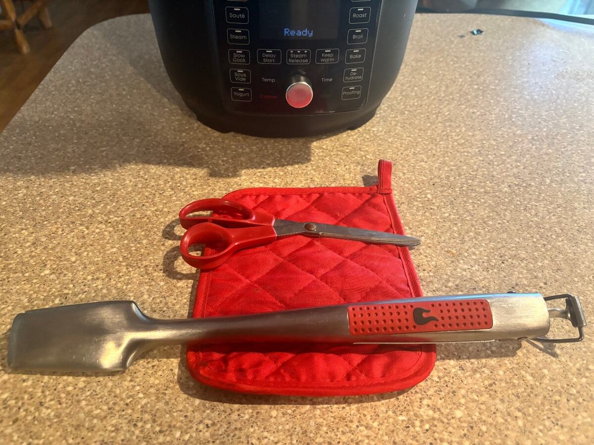 steel spatula and scissors on top of red oven mitts