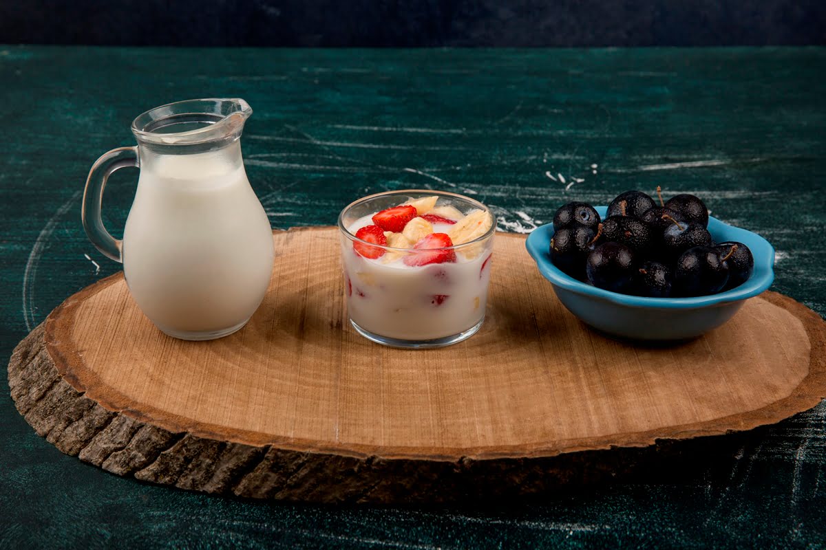 strawberries in yogurt served with milk and cherries on a wooden platter