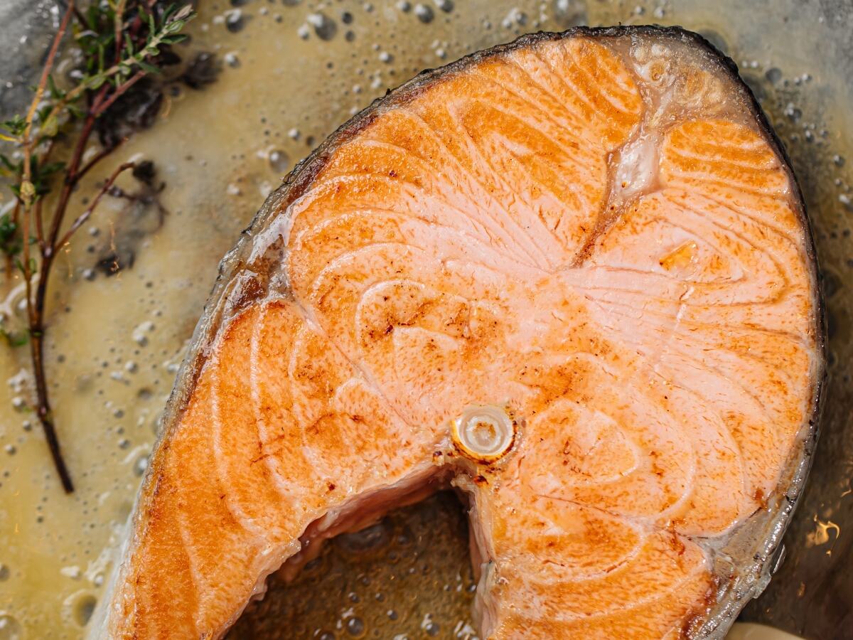 Frying salmon steak on parchment paper with butter and rosemary