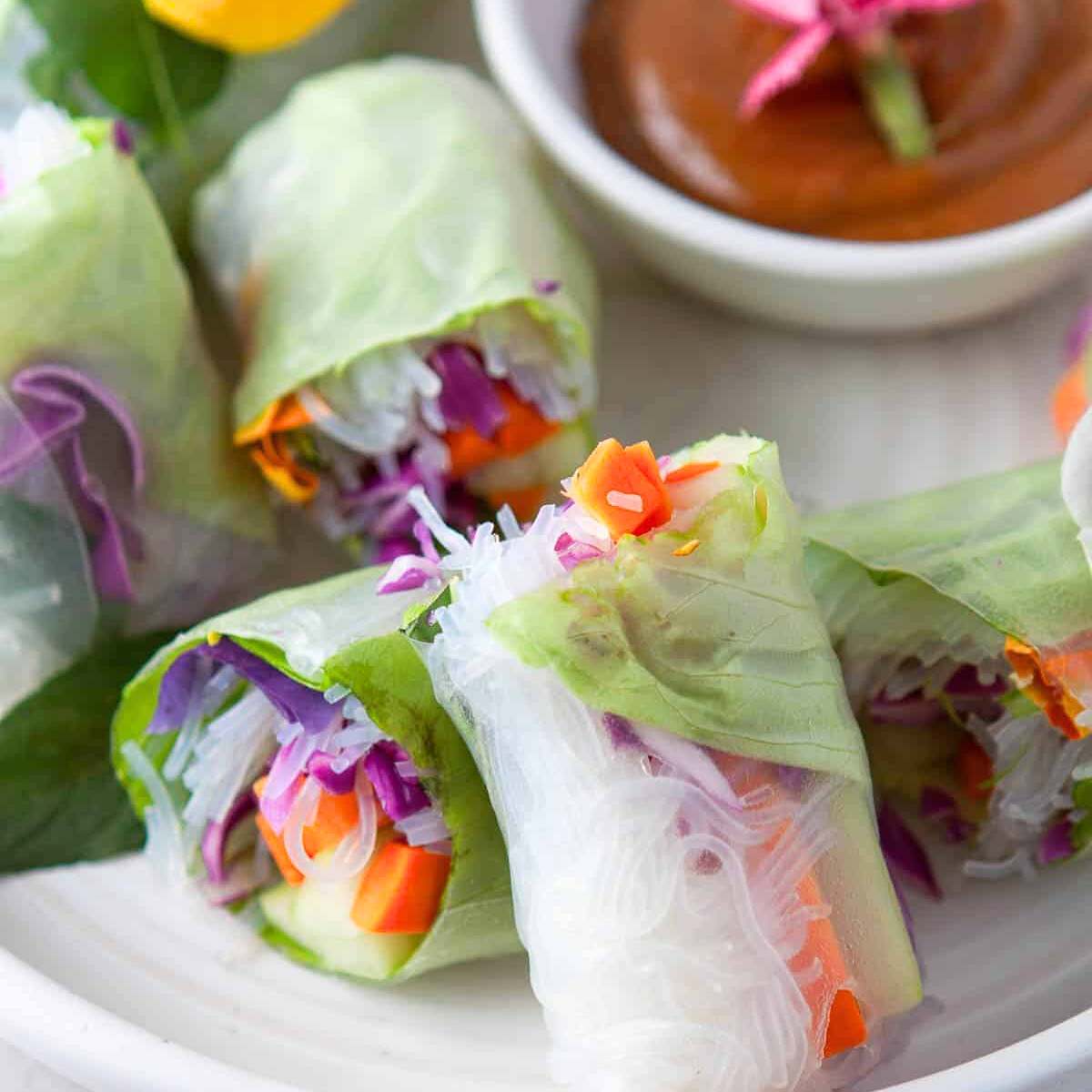 A plate of colorful spring rolls made with rice paper, filled with rice noodles, shredded vegetables, and herbs. Served with a dipping sauce.