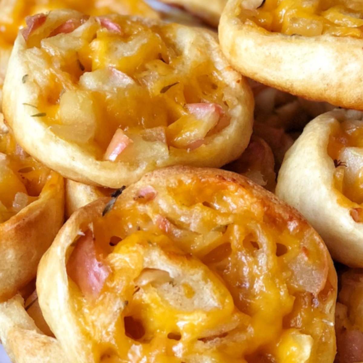  A close-up photo of baked apple cheddar pinwheels, showing the flaky pastry, melted cheese, and visible apple slices.