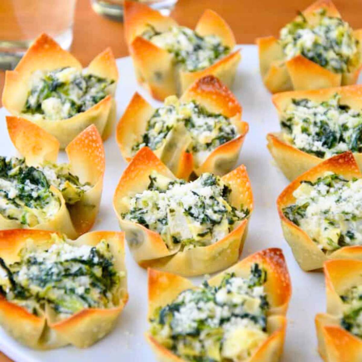  A platter of baked wonton cups filled with a creamy spinach and artichoke dip, topped with shredded Parmesan cheese.