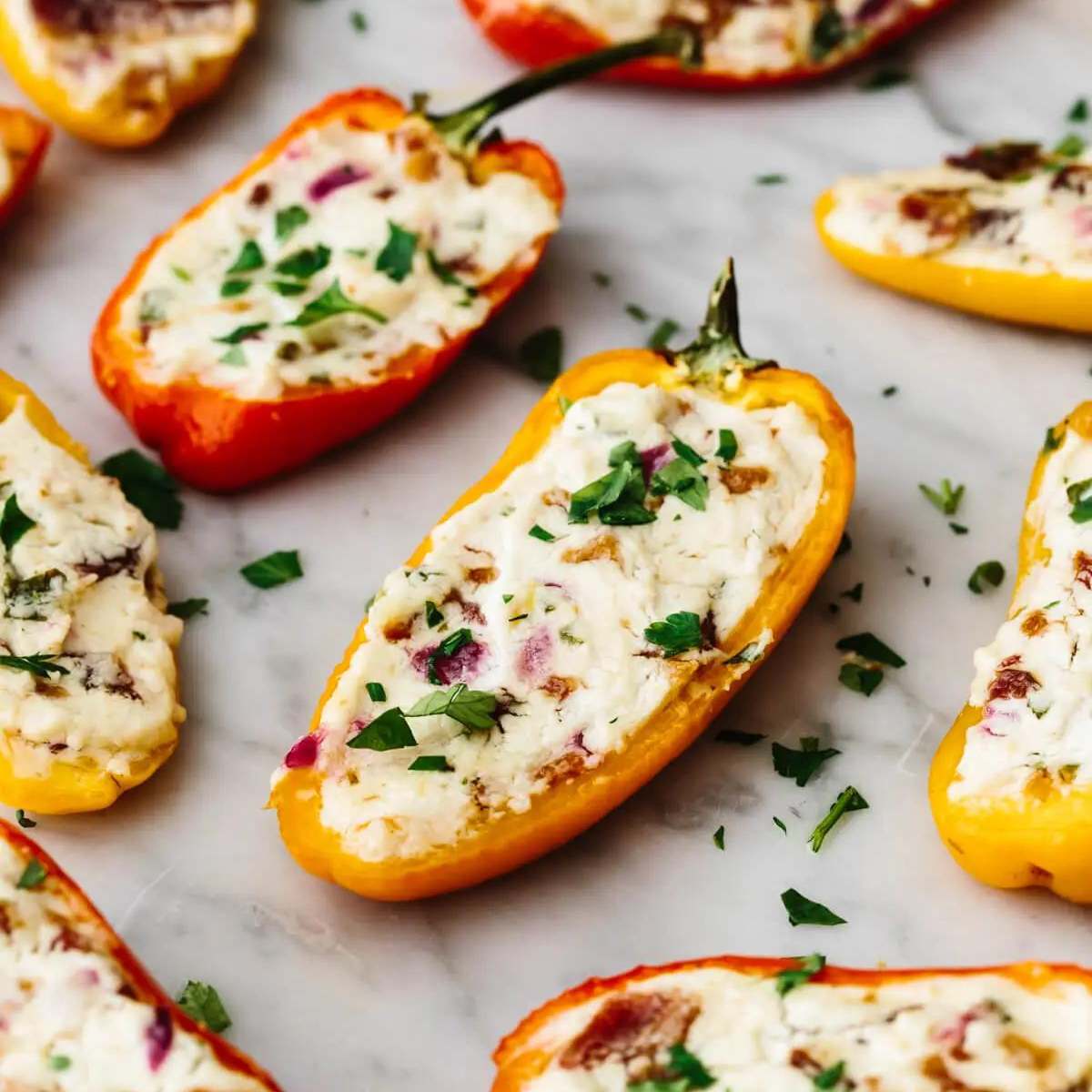 Several mini bell peppers stuffed with a creamy cheese mixture and topped with crumbled bacon and fresh parsley.