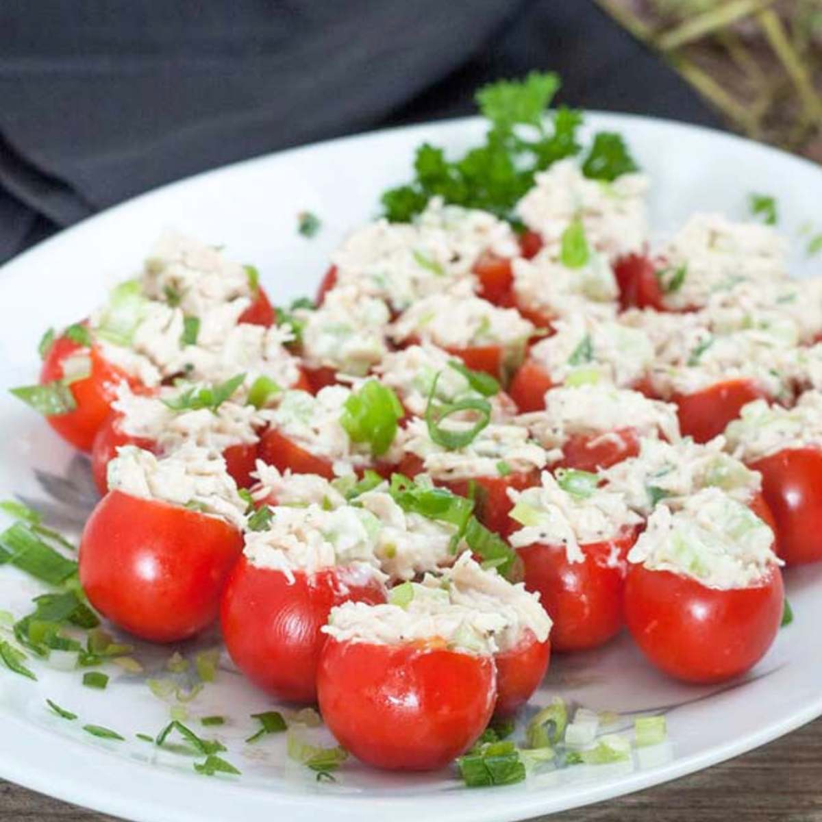 A platter of cherry tomatoes stuffed with a creamy chicken salad mixture, garnished with chopped green onions and fresh parsley.