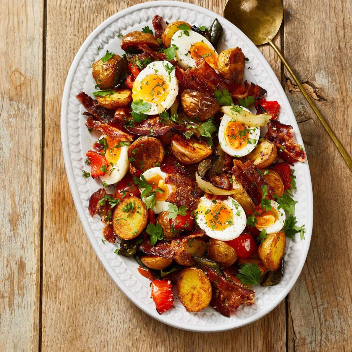 A salad with roasted potatoes, bacon, hard-boiled eggs, and vegetables served on a white oval plate.