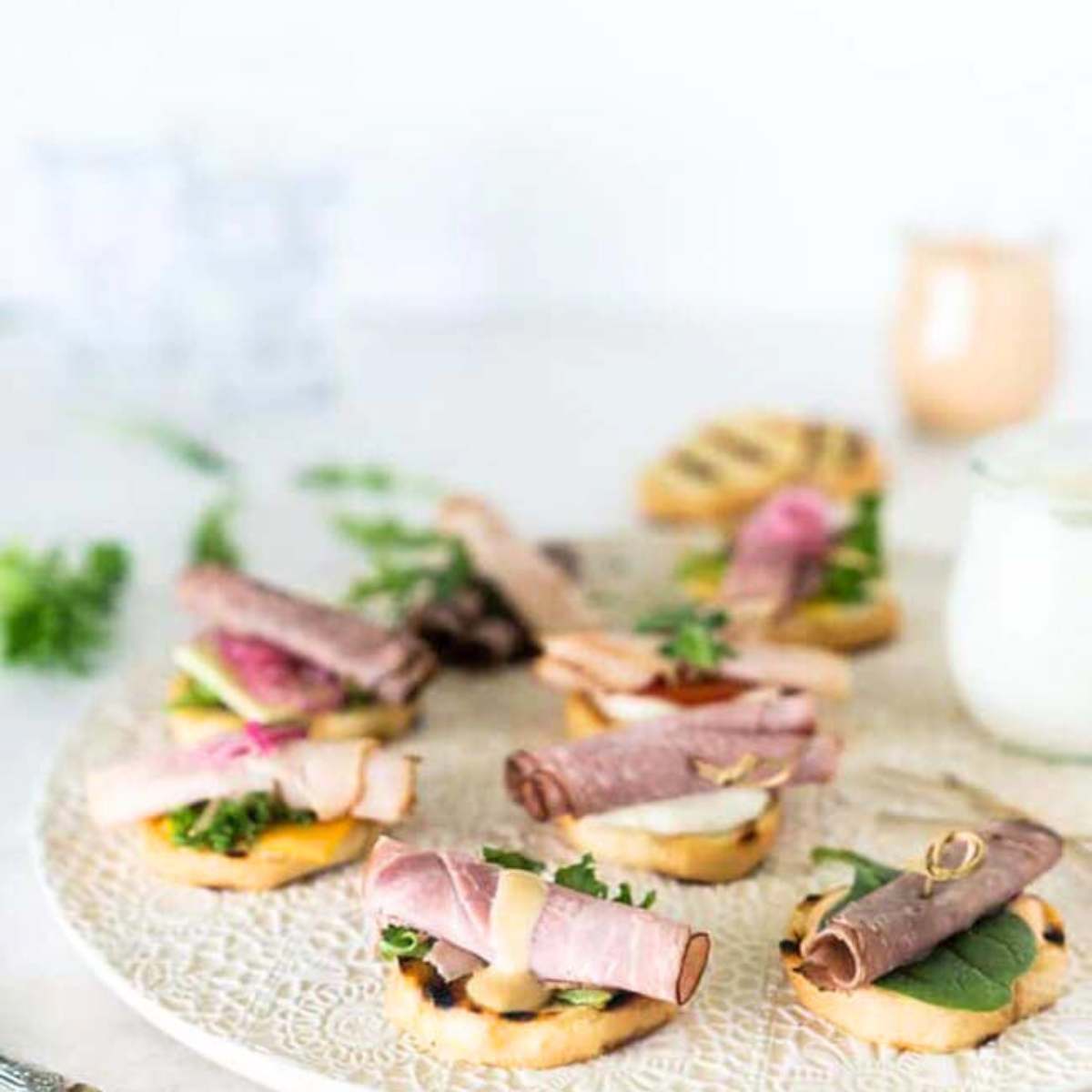 A plate of grilled crostini topped with various deli meats, cheese, and vegetables. 