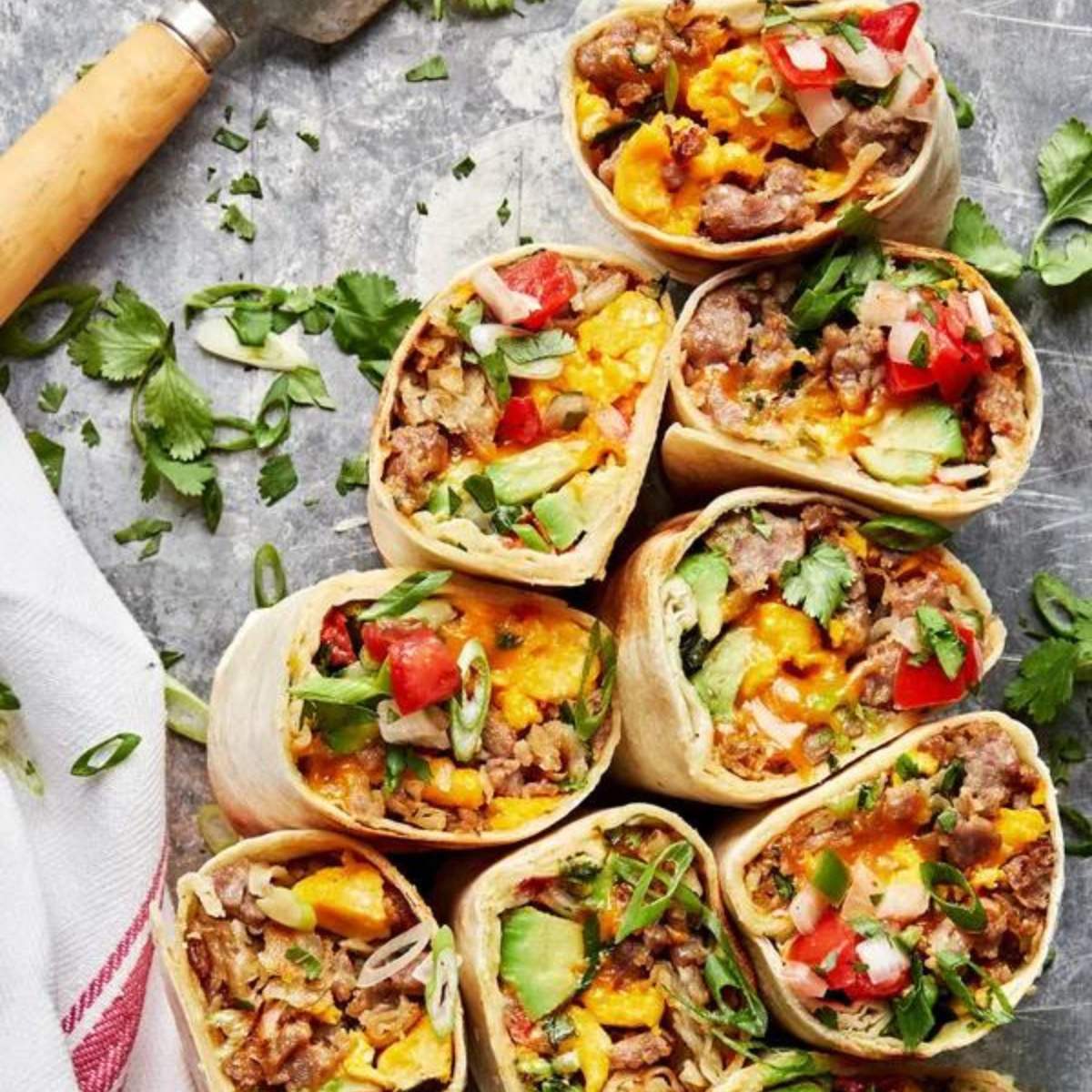  Several breakfast burritos filled with scrambled eggs, sausage, cheese, and vegetables, served with salsa and avocado.