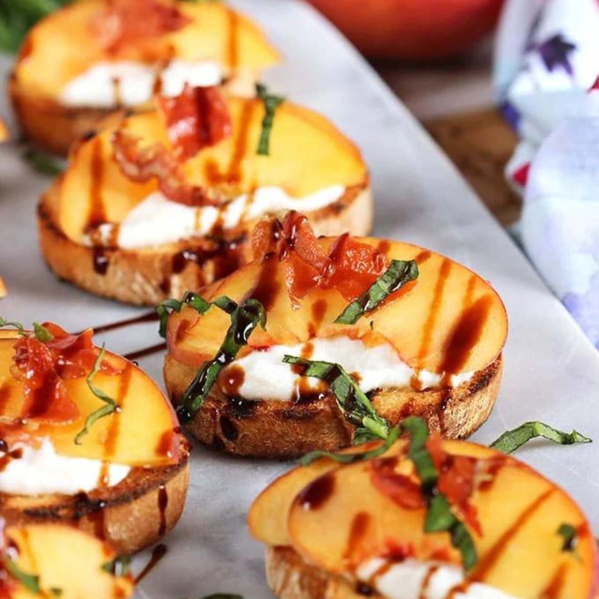  A platter of crispy crostini topped with creamy ricotta, fresh peach slices, crispy pancetta, and a drizzle of balsamic glaze.