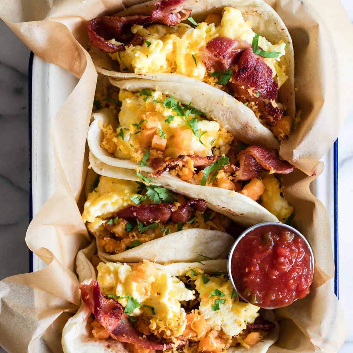  Breakfast tacos filled with scrambled eggs, bacon, and potatoes, served with salsa.