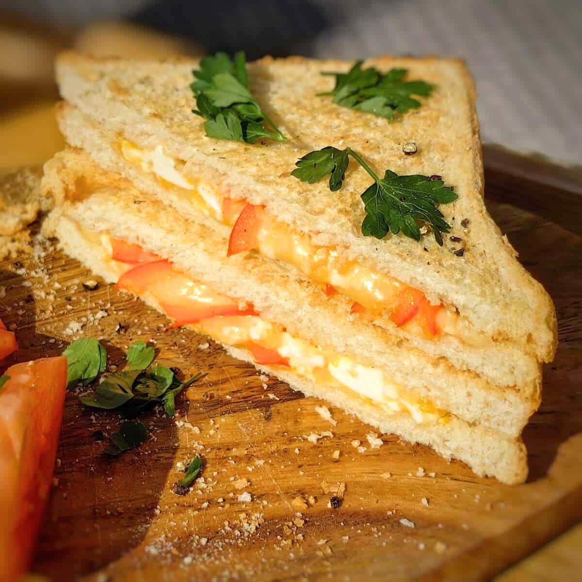  A grilled sandwich with egg, cheese, and tomato slices, garnished with fresh parsley.