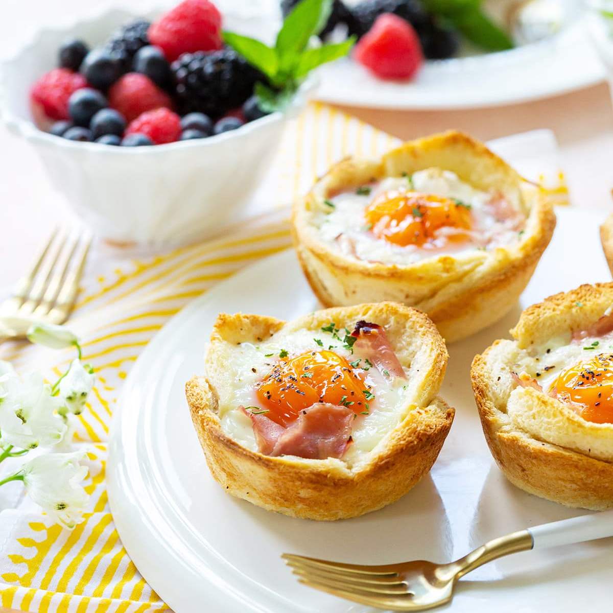 A plate of three Croque Madame breakfast cups. Each cup is made from a hollowed-out bread slice, filled with ham and cheese, and topped with a fried egg. 