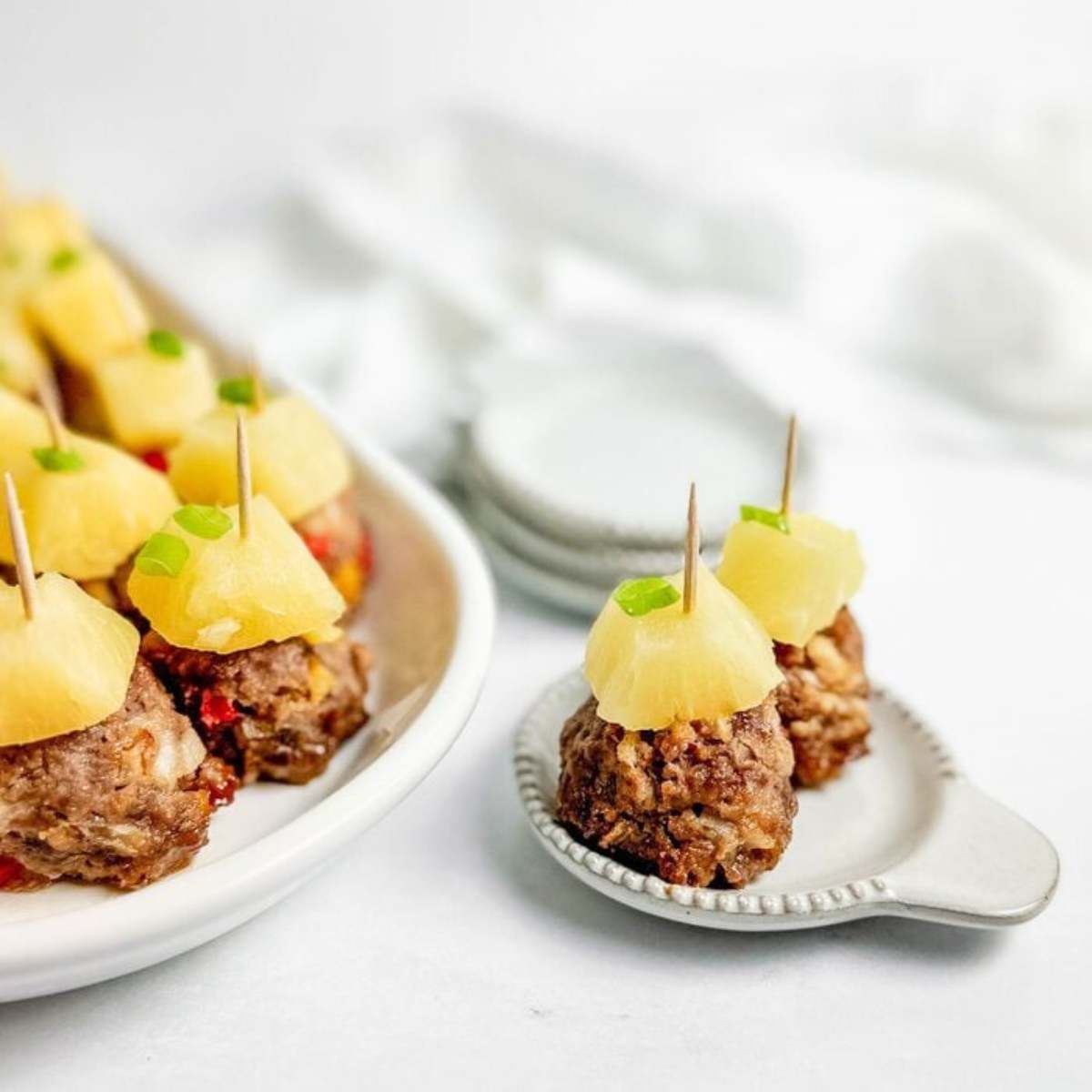 Small meatballs topped with pineapple chunks and green onion on a white plate

