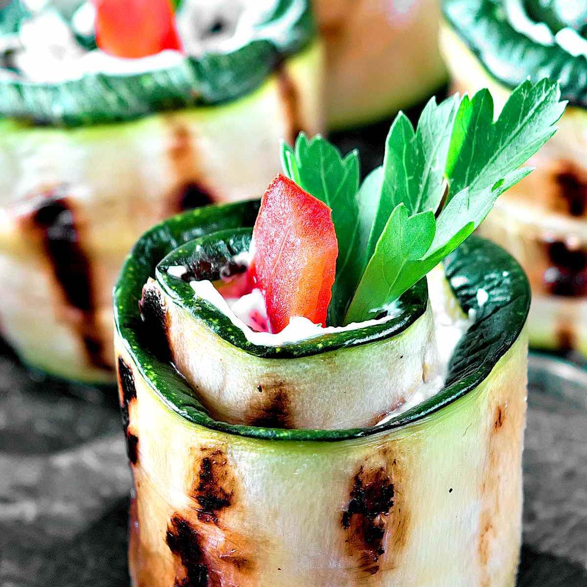 Grilled zucchini slices rolled up and filled with a creamy filling, garnished with fresh parsley and a red pepper slice. cold appetizer recipes