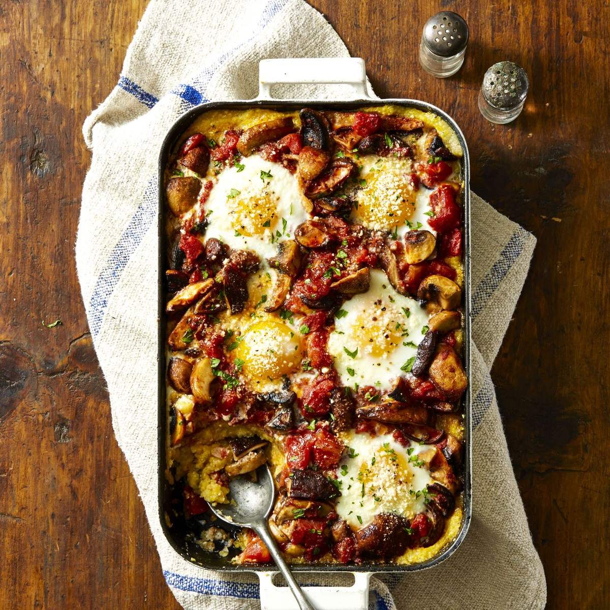 Baked egg dish with mushrooms, tomatoes, and herbs in a white rectangular casserole dish.