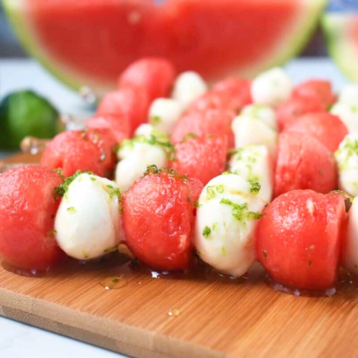  A wooden board filled with skewers of watermelon and mozzarella balls, drizzled with honey lime dressing.