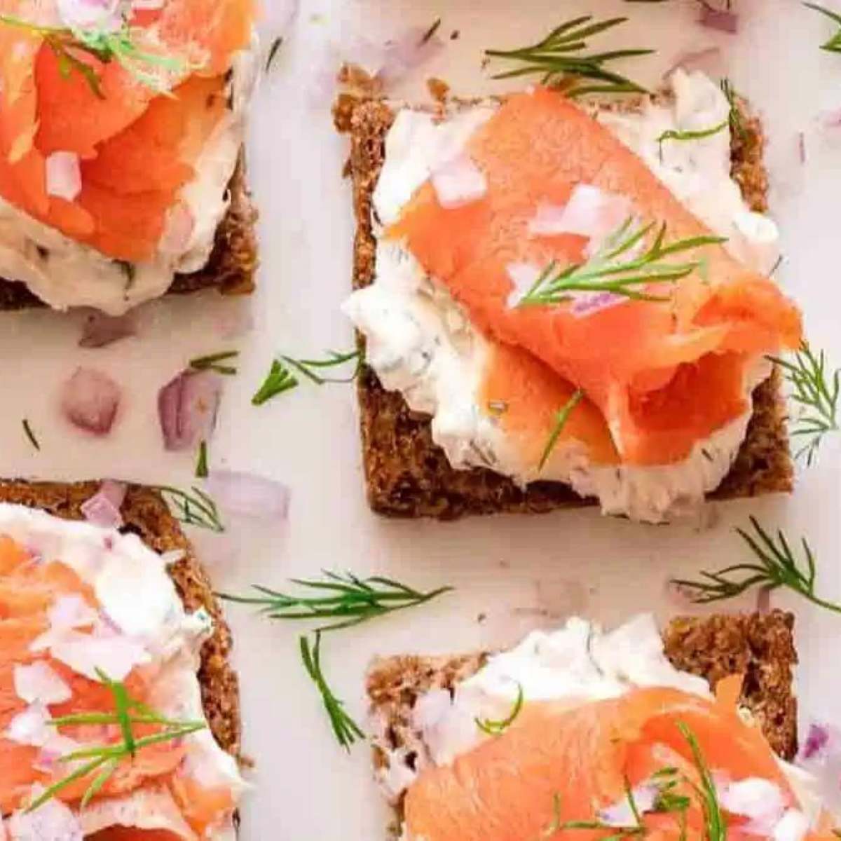  A plate of smoked salmon canapés with cream cheese, red onion, and dill on rye bread.