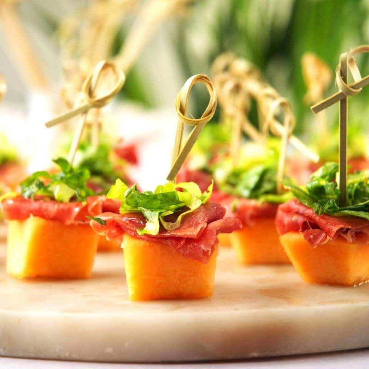 A platter of melon and prosciutto skewers on a marble board.