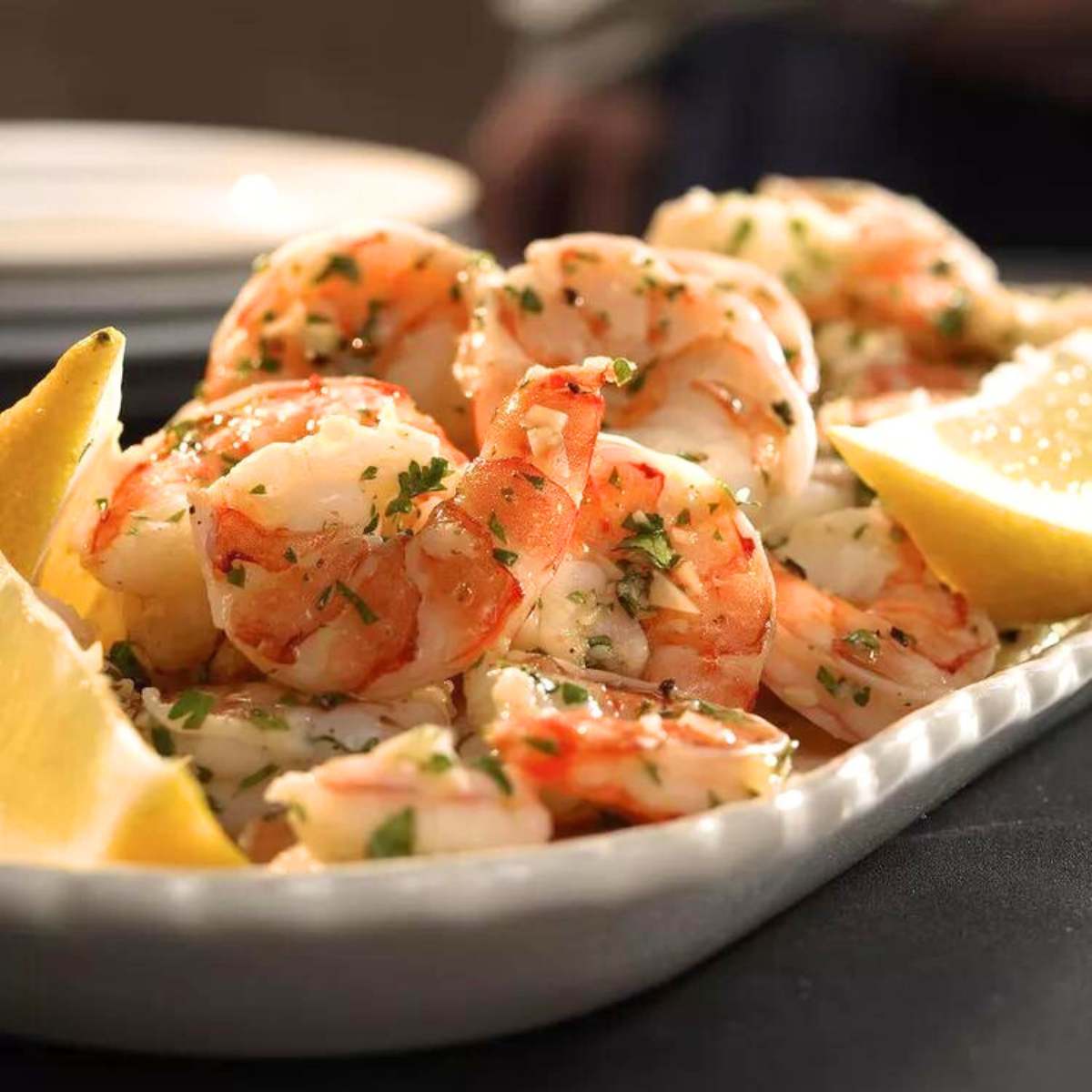 Cooked shrimp, seasoned with garlic and parsley, and lemon wedges served on a white platter.