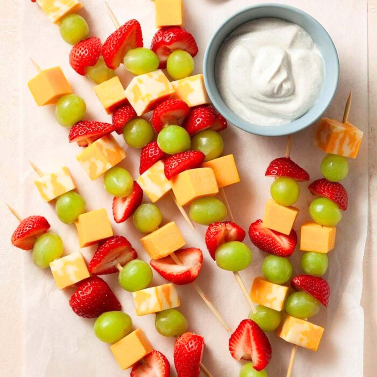 A plate of fruit and cheese skewers, featuring strawberries, grapes, and cubes of cheese. 