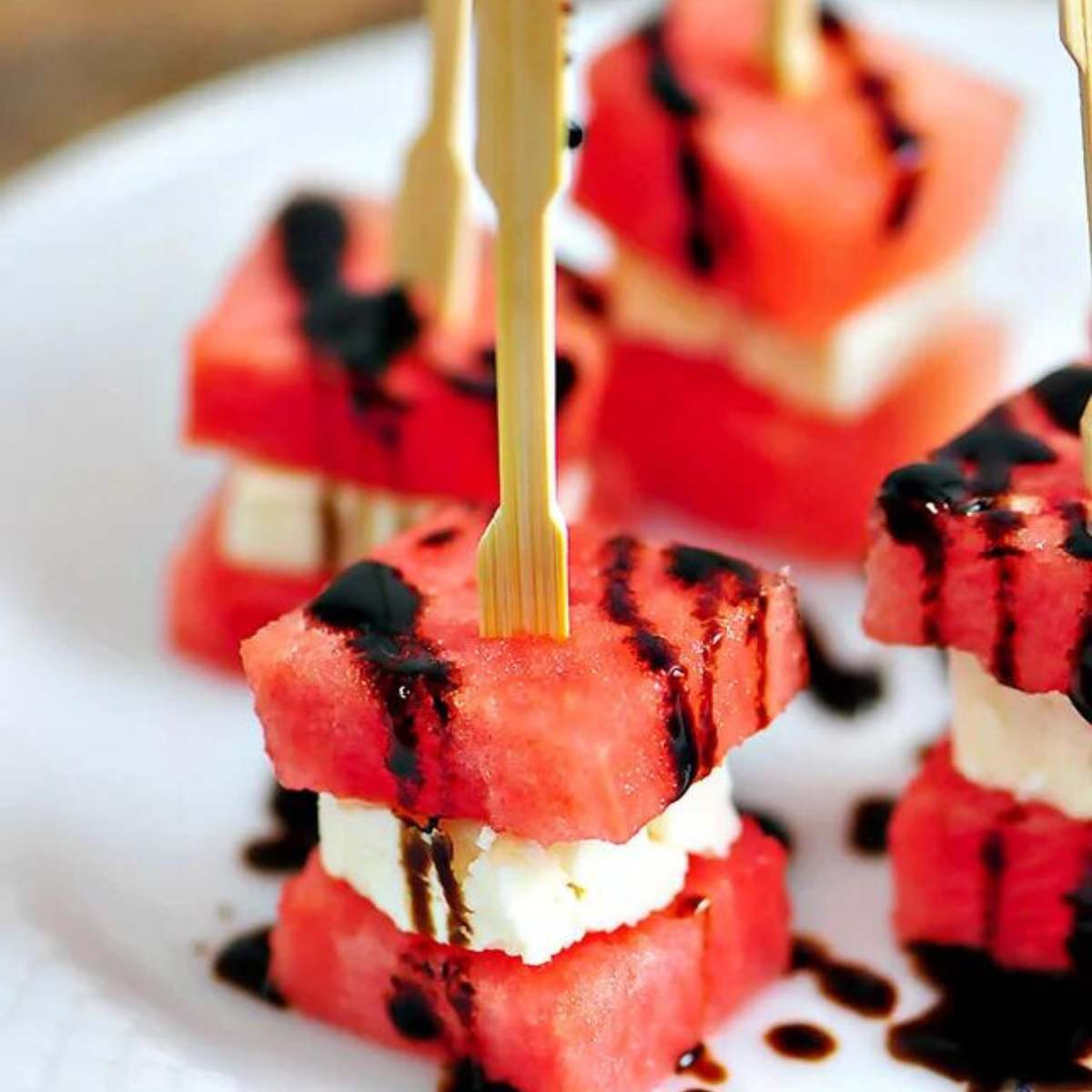 A plate of watermelon and feta cheese skewers, drizzled with balsamic glaze.