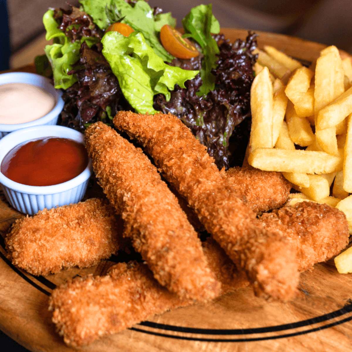 A plate of crispy chicken fries served with French fries and a side salad, with ketchup and mayonnaise dipping sauces.