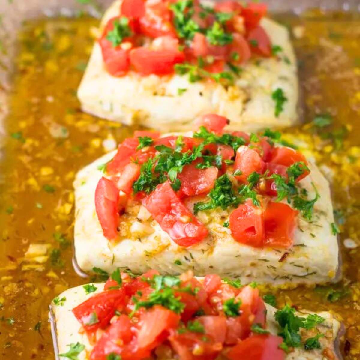 Baked white fish topped with a tomato and garlic sauce, garnished with fresh parsley.

