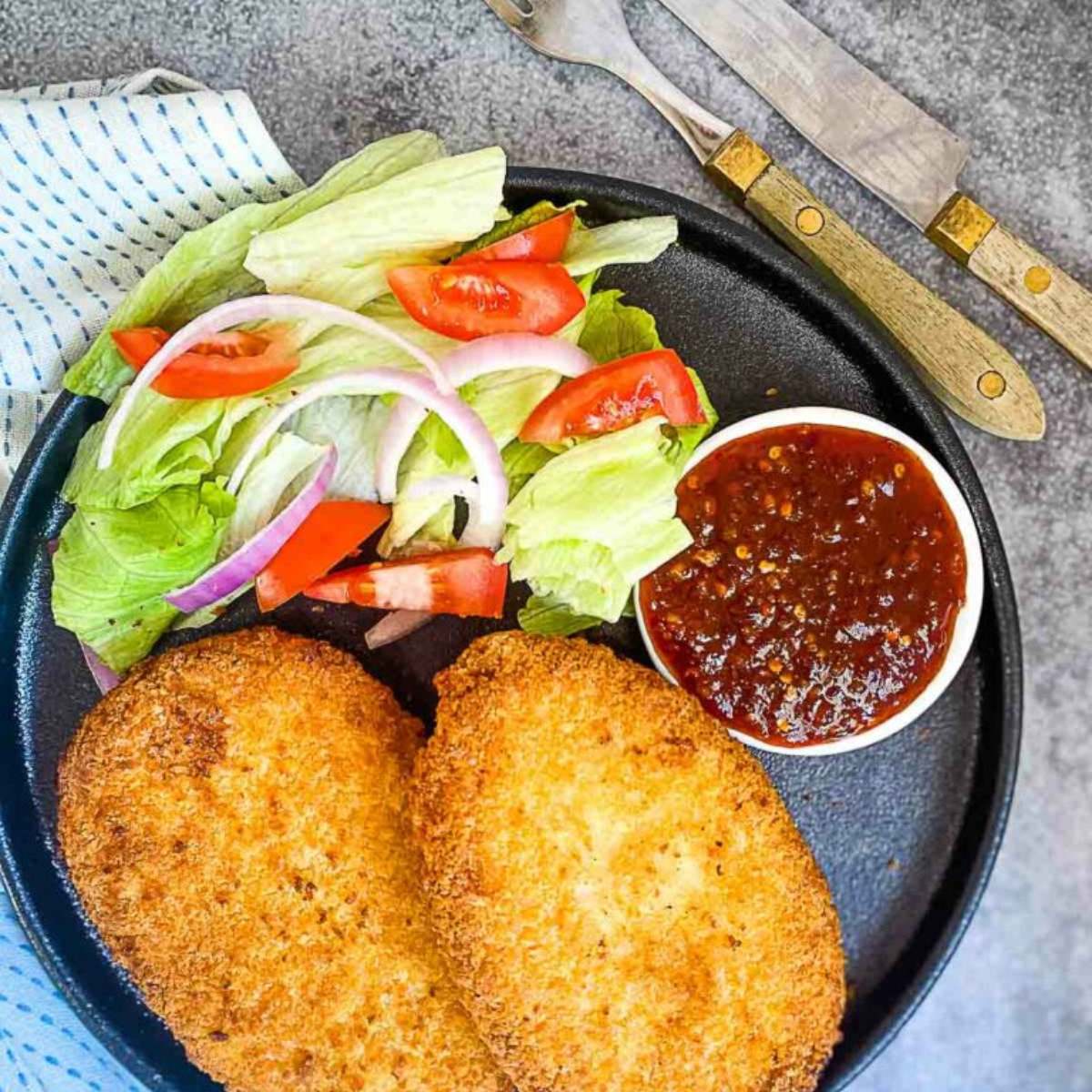 Two breaded chicken breasts cooked in an air fryer, served with a side salad and a small bowl of dipping sauce.