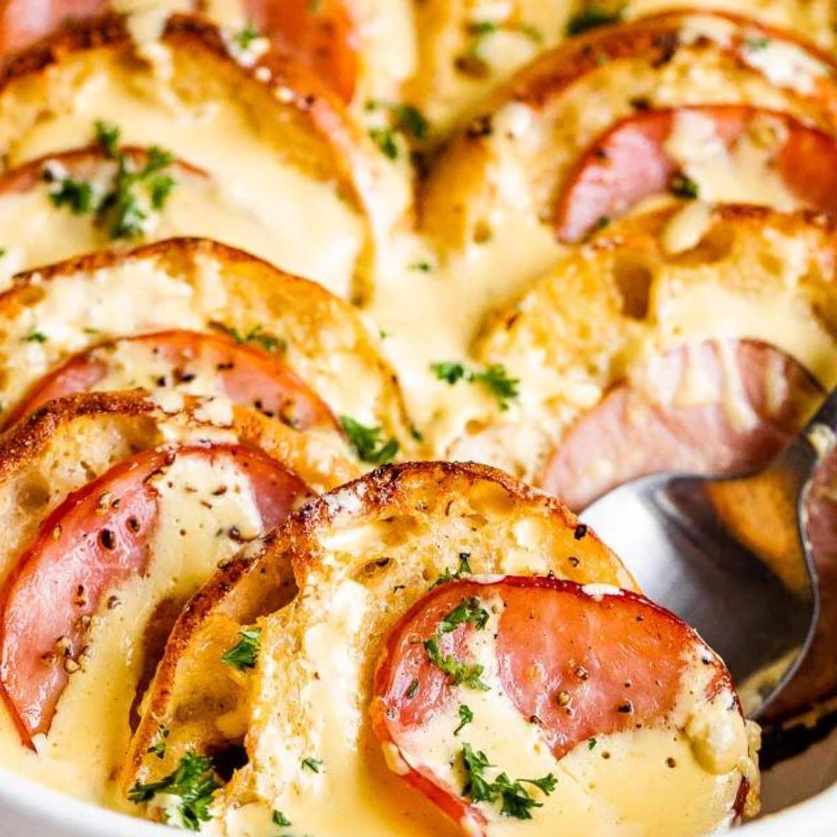 A baked casserole with bread, ham, and cheese, topped with a creamy sauce and fresh parsley.

