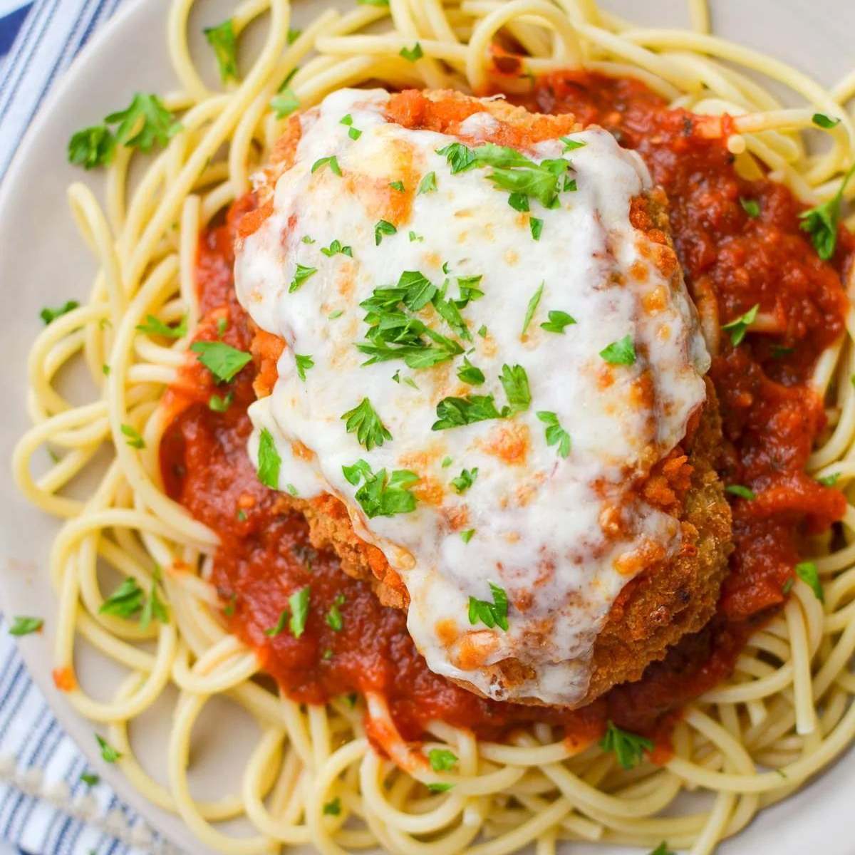 Air fryer chicken parmesan served over spaghetti noodles with marinara sauce, topped with melted mozzarella cheese and fresh parsley.