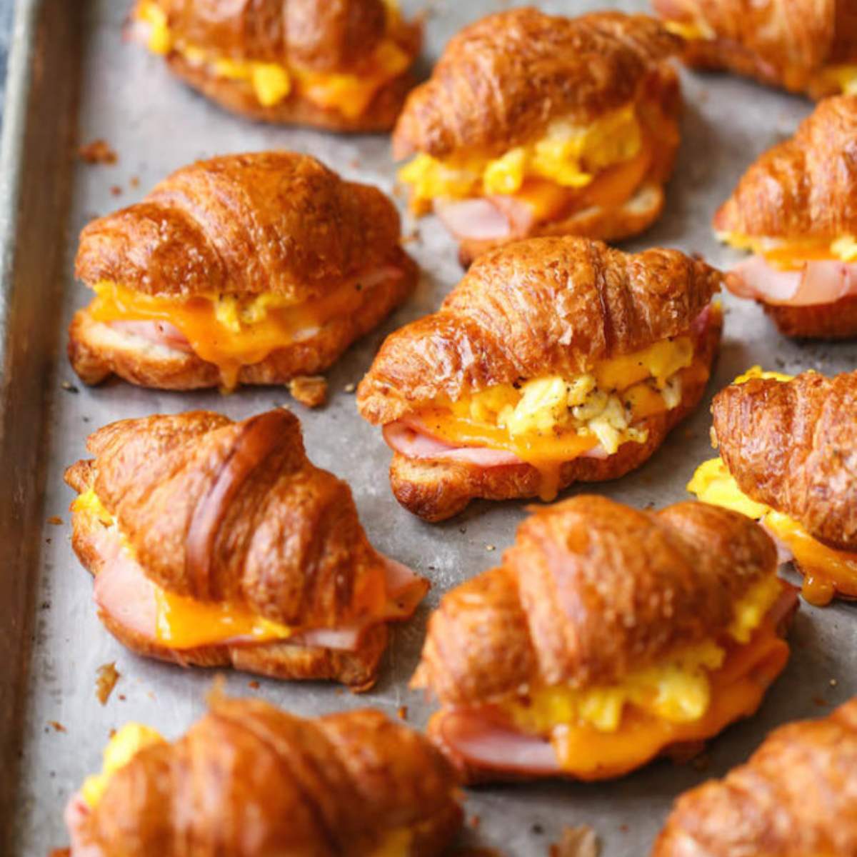  A baking sheet filled with mini croissants filled with ham, cheese, and scrambled eggs.

