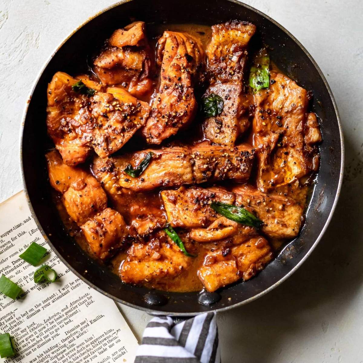  A skillet filled with pan-fried fish with a spicy, tangy sauce and scattered with green onion leaves.

