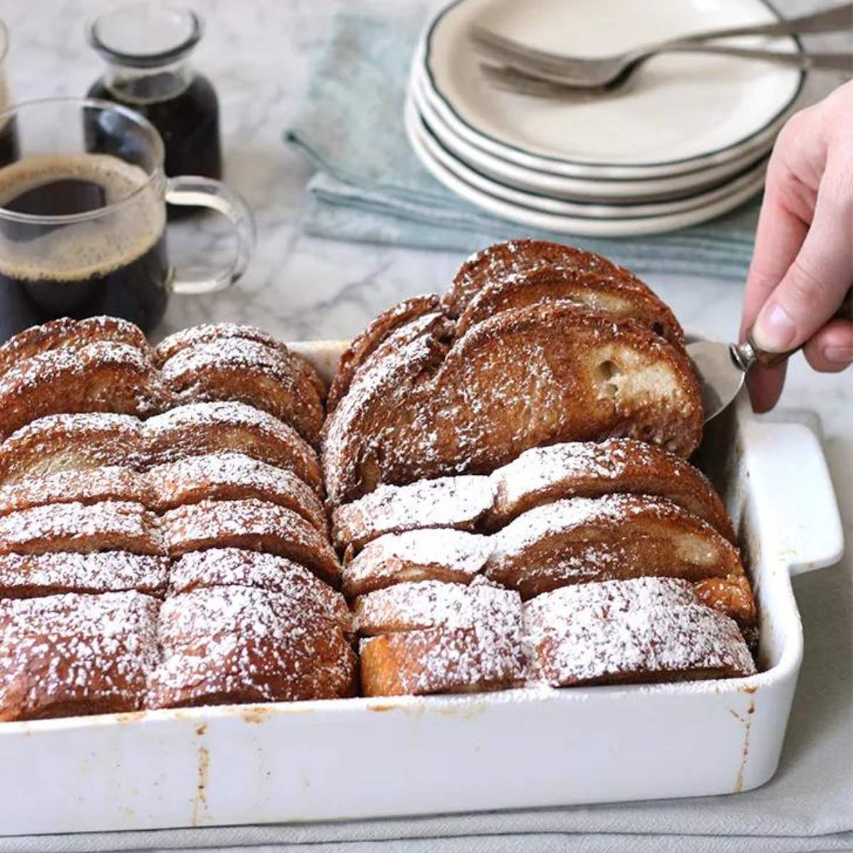  Baked French toast with powdered sugar, served in a white dish.

