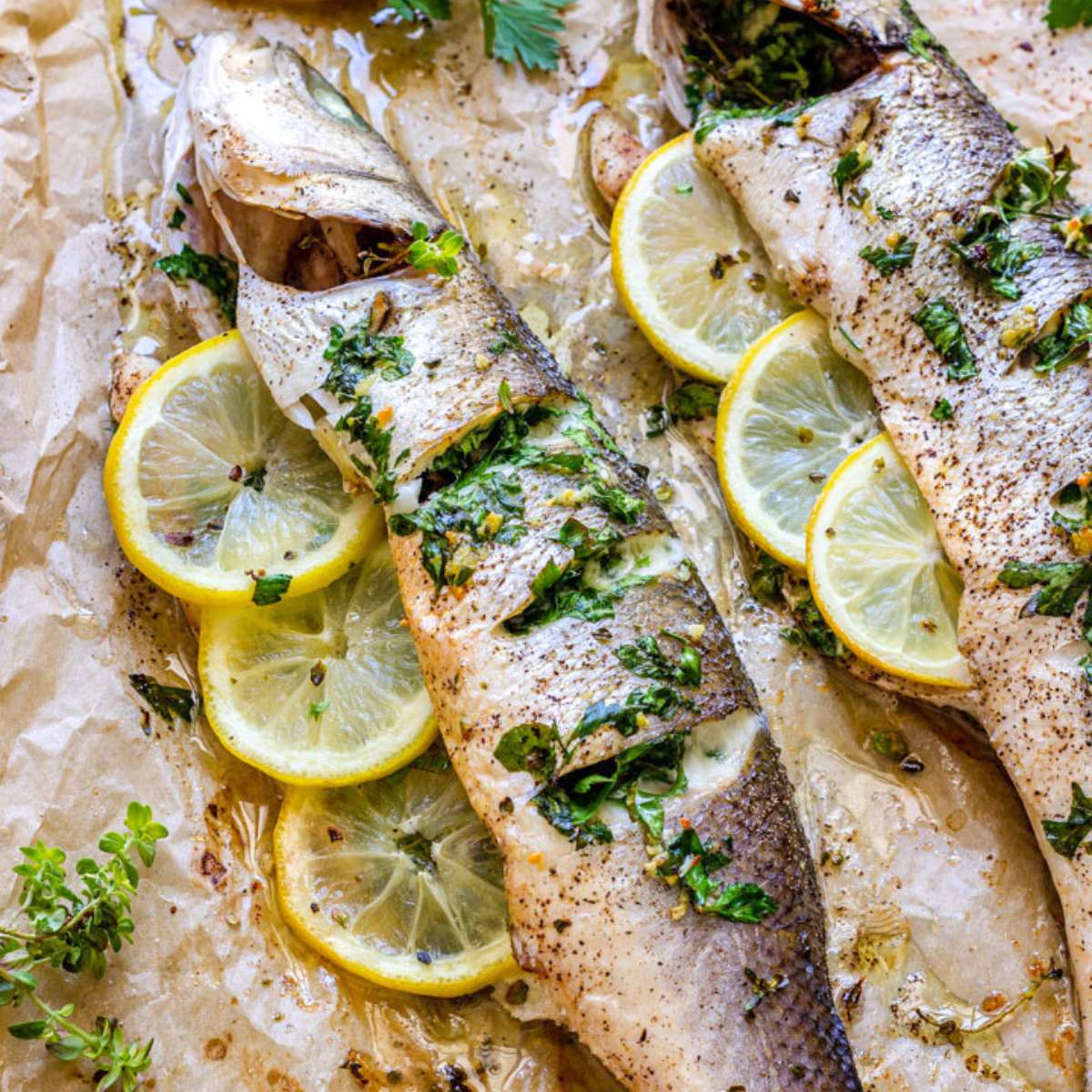  Two whole cooked fish stuffed with lemon slices, herbs, and spices, baked on a sheet pan.

