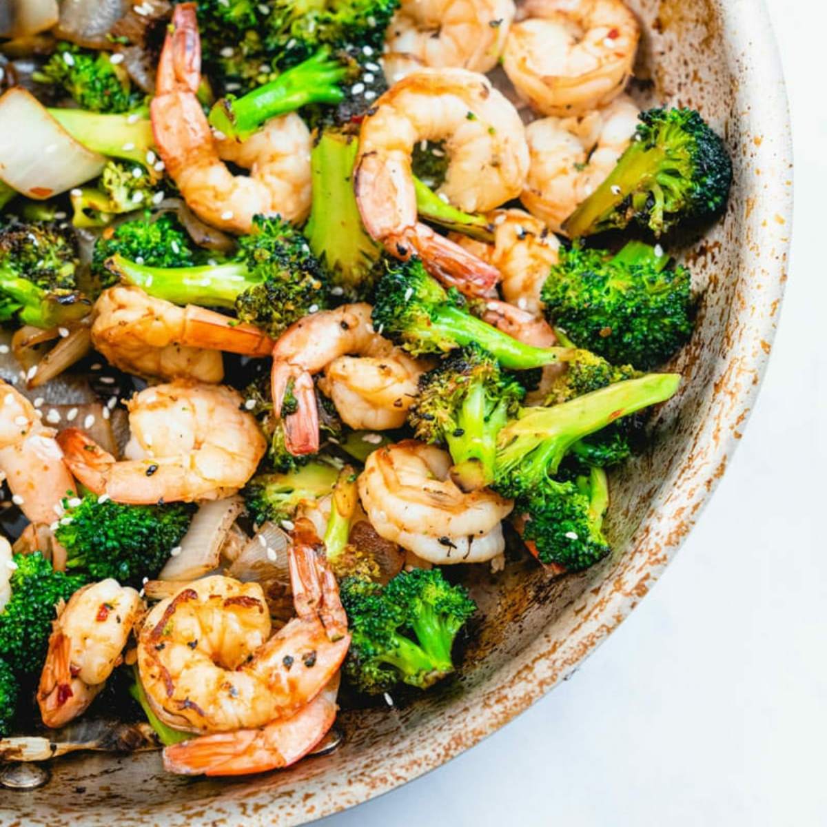 Stir-fried shrimp and broccoli in a bowl.  Sesame seeds are sprinkled on top.