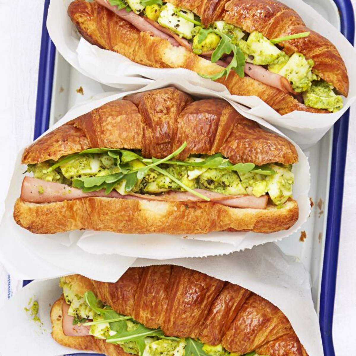 Croissants filled with ham, egg salad, and arugula, wrapped in parchment paper.