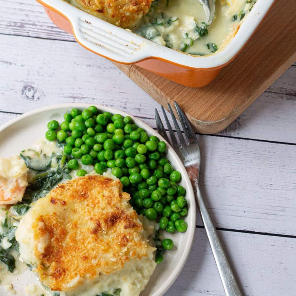 Fish pie with a creamy spinach and cheese filling, topped with a golden crust. Served with a side of peas.

