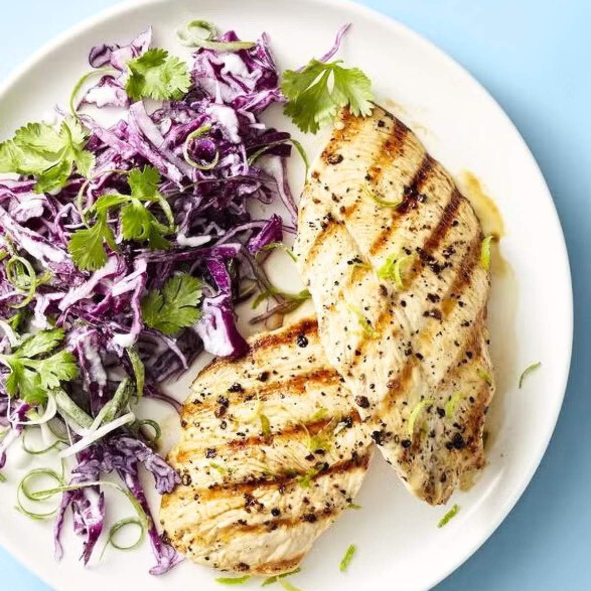 Grilled chicken breasts served with a side of red cabbage slaw. The chicken is seasoned with herbs and spices and has visible grill marks.

