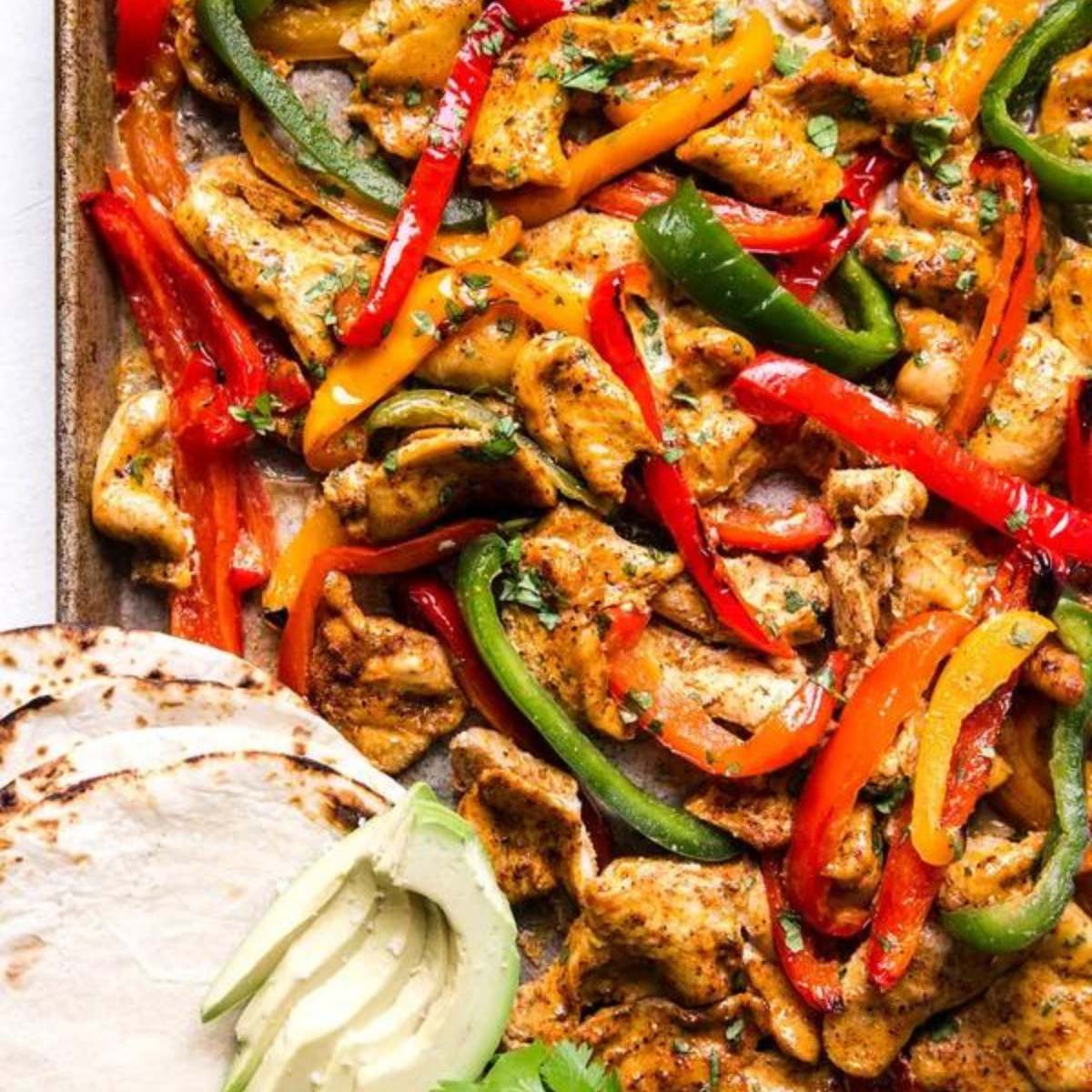  Sheet pan chicken fajitas with grilled chicken, bell peppers, and onions, served with tortillas and avocado slices.