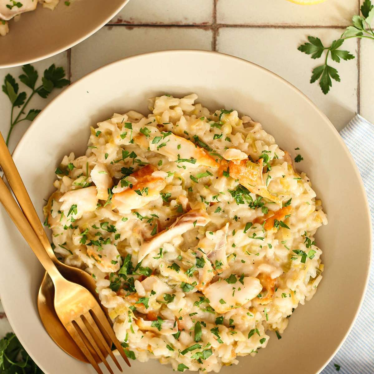 Creamy risotto with flaked white fish and fresh parsley served on a white bowl.