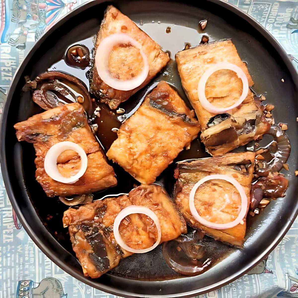 Fried fish fillets served on a black plate with a black sauce and onion rings.