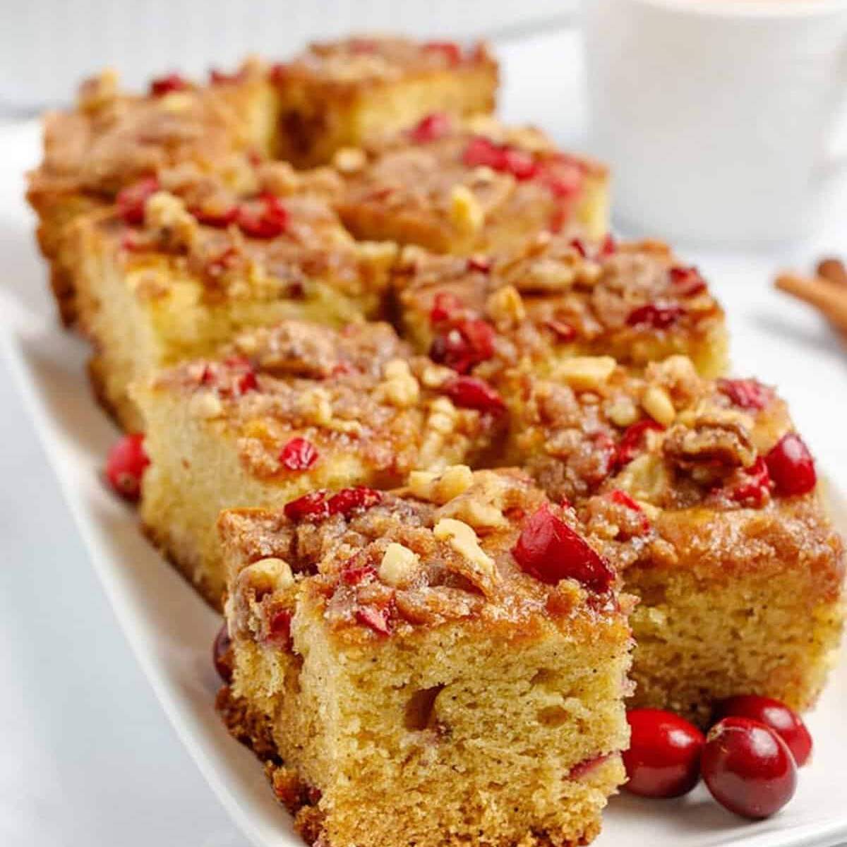  A platter of cranberry coffee cake squares with a streusel topping, served with fresh cranberries and cinnamon sticks.