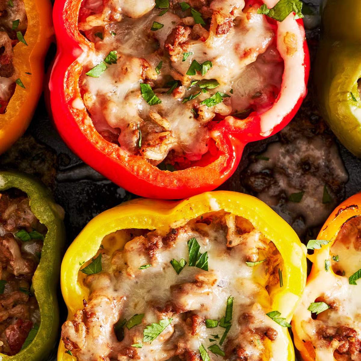 Stuffed bell peppers with ground beef, rice, and melted cheese. The peppers are in various colors and are topped with fresh parsley.