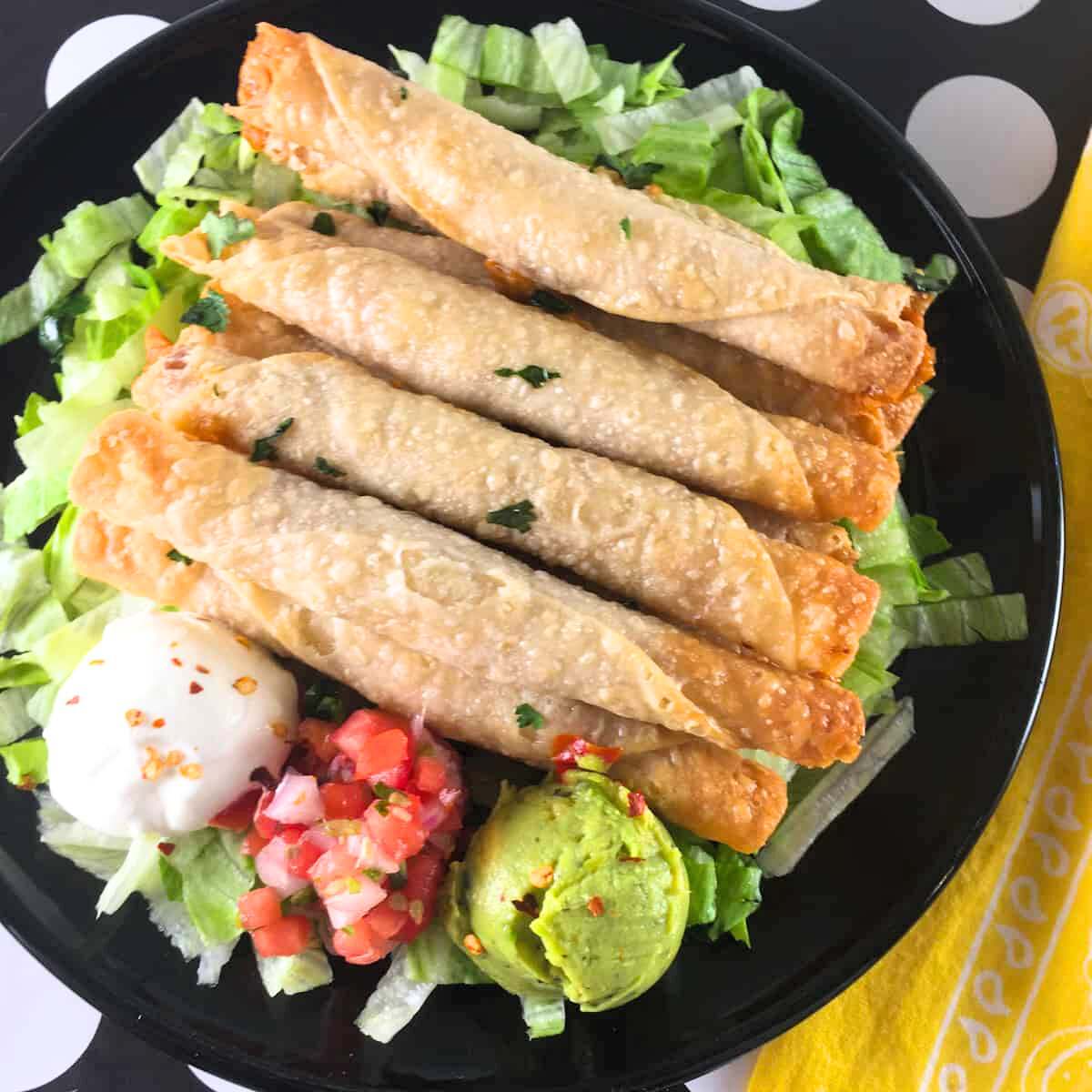  Air fryer frozen taquitos served on a bed of lettuce with salsa, guacamole, and sour cream.